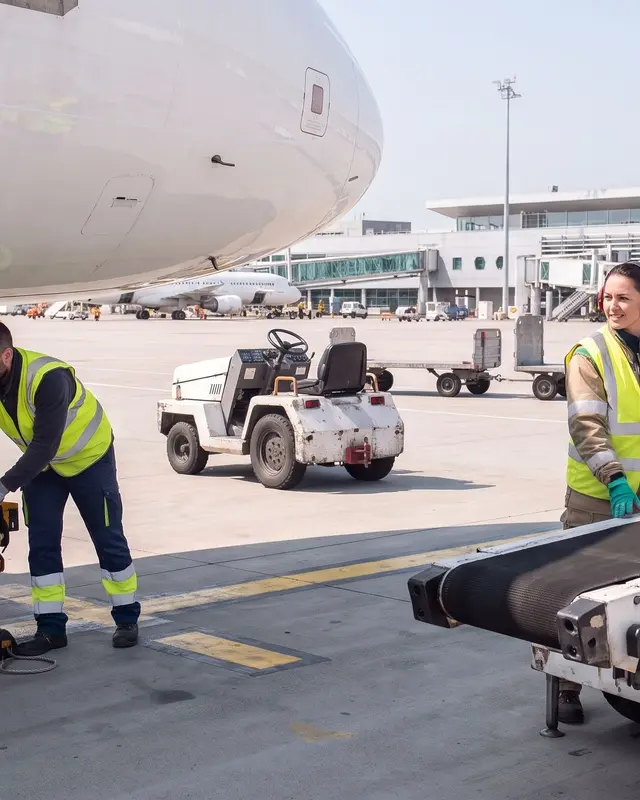 Deux agents de piste en gilet de sécurité travaillent près d'un avion sur le tarmac.