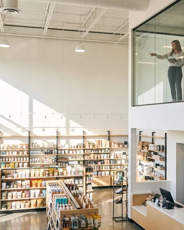 Une directrice et sa collaboratrice observent l'activité d'un magasin de retail moderne depuis une mezzanine vitrée.