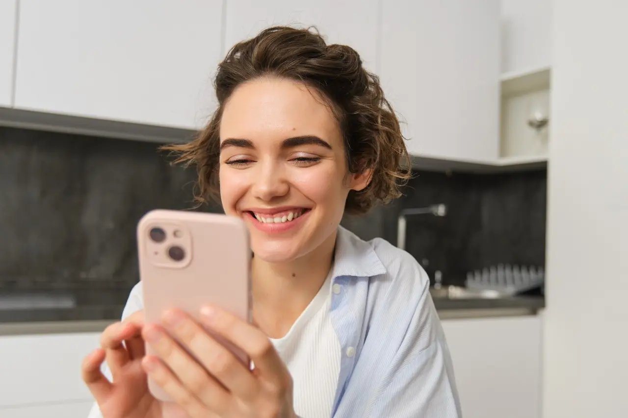 Une jeune femme souriante gère son épargne sur son smartphone.