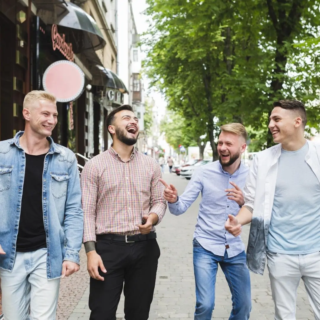 Quatre jeunes hommes souriants marchent et rient ensemble dans la rue.
