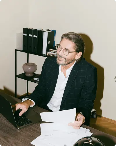 Un professionnel souriant travaille à son bureau avec un ordinateur portable et des documents.