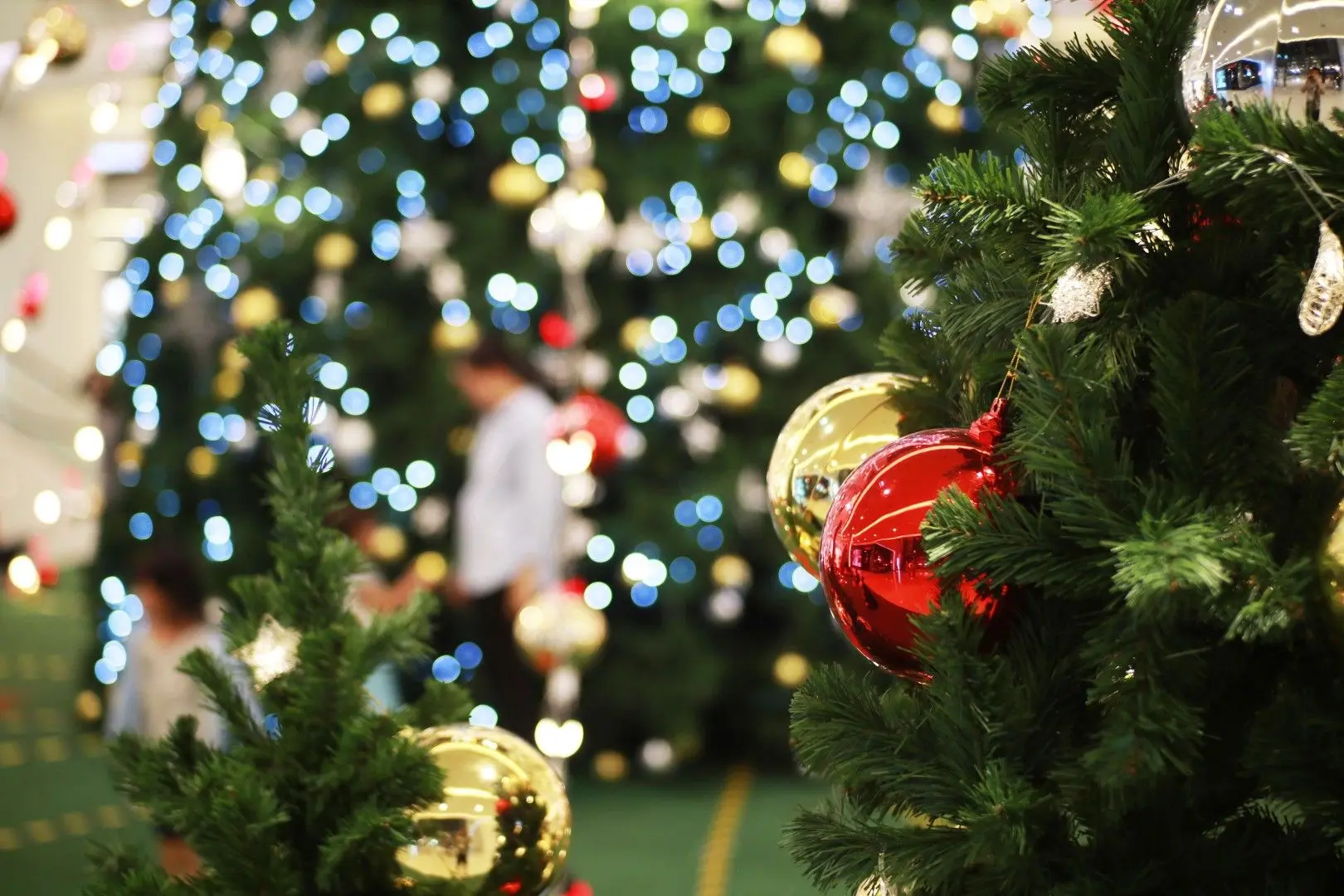 Sapin de Noël décoré de boules rouge et dorée avec des illuminations festives floues en arrière-plan.