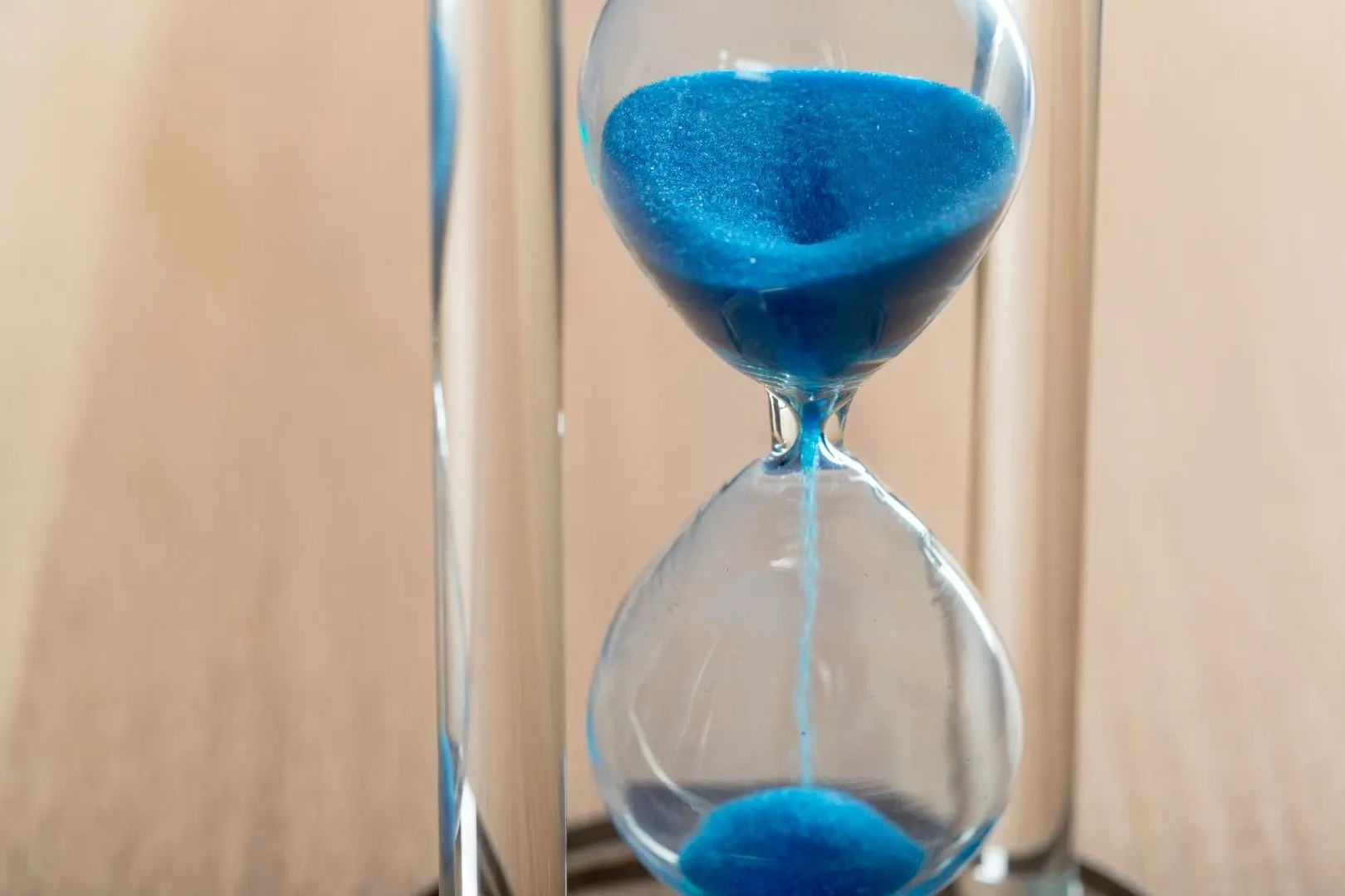 Un sablier en verre avec du sable bleu qui s'écoule.