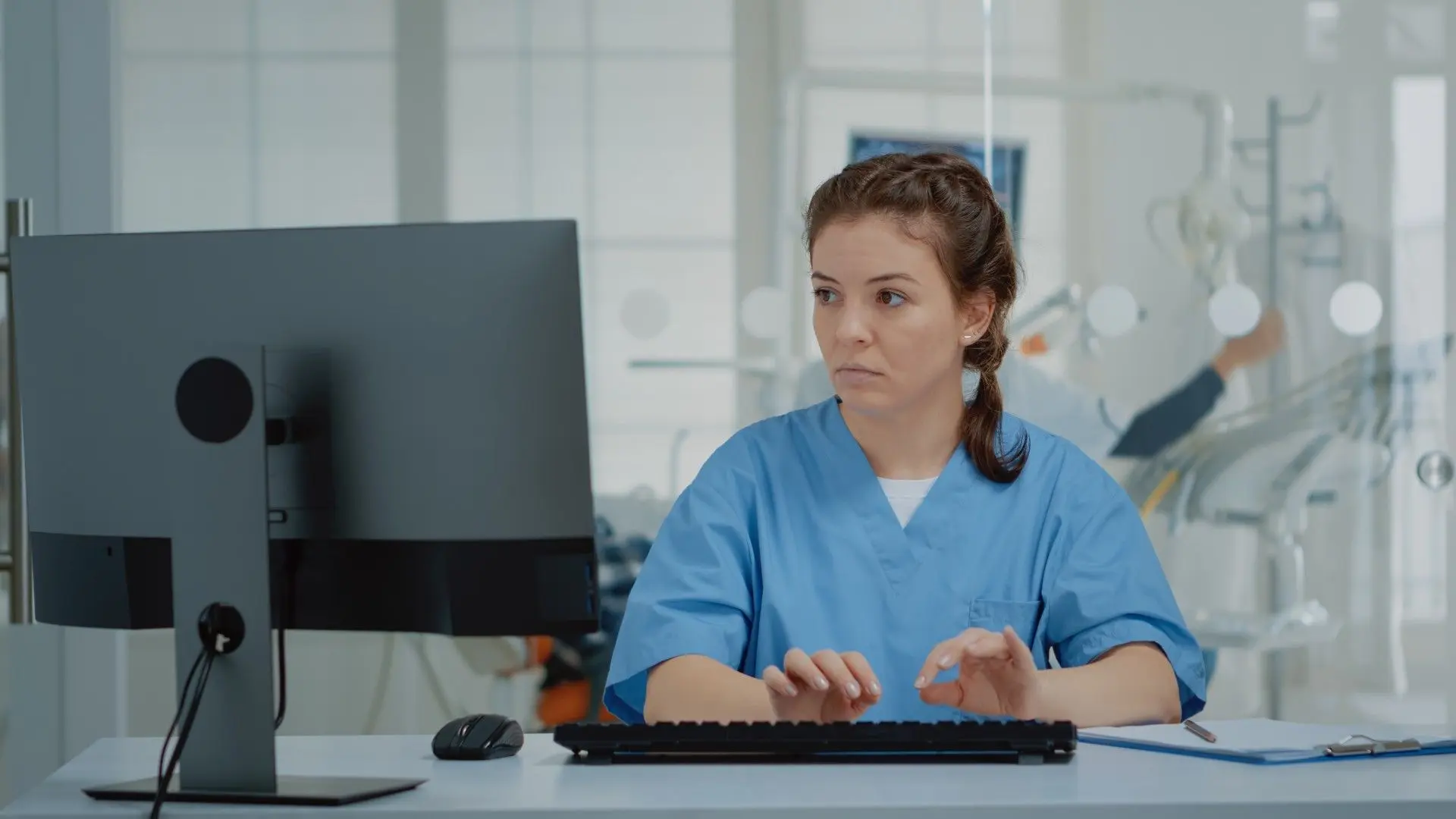 Une dosimétriste en blouse médicale bleue saisit des données sur son ordinateur de bureau.