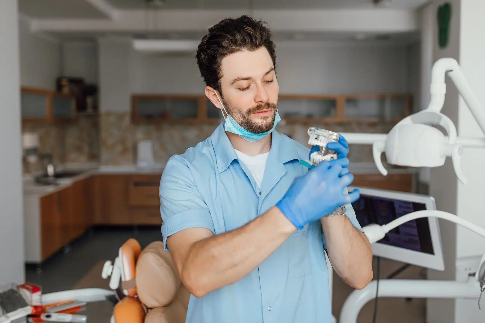Un prothésiste dentaire en blouse bleue examine un modèle de mâchoire.