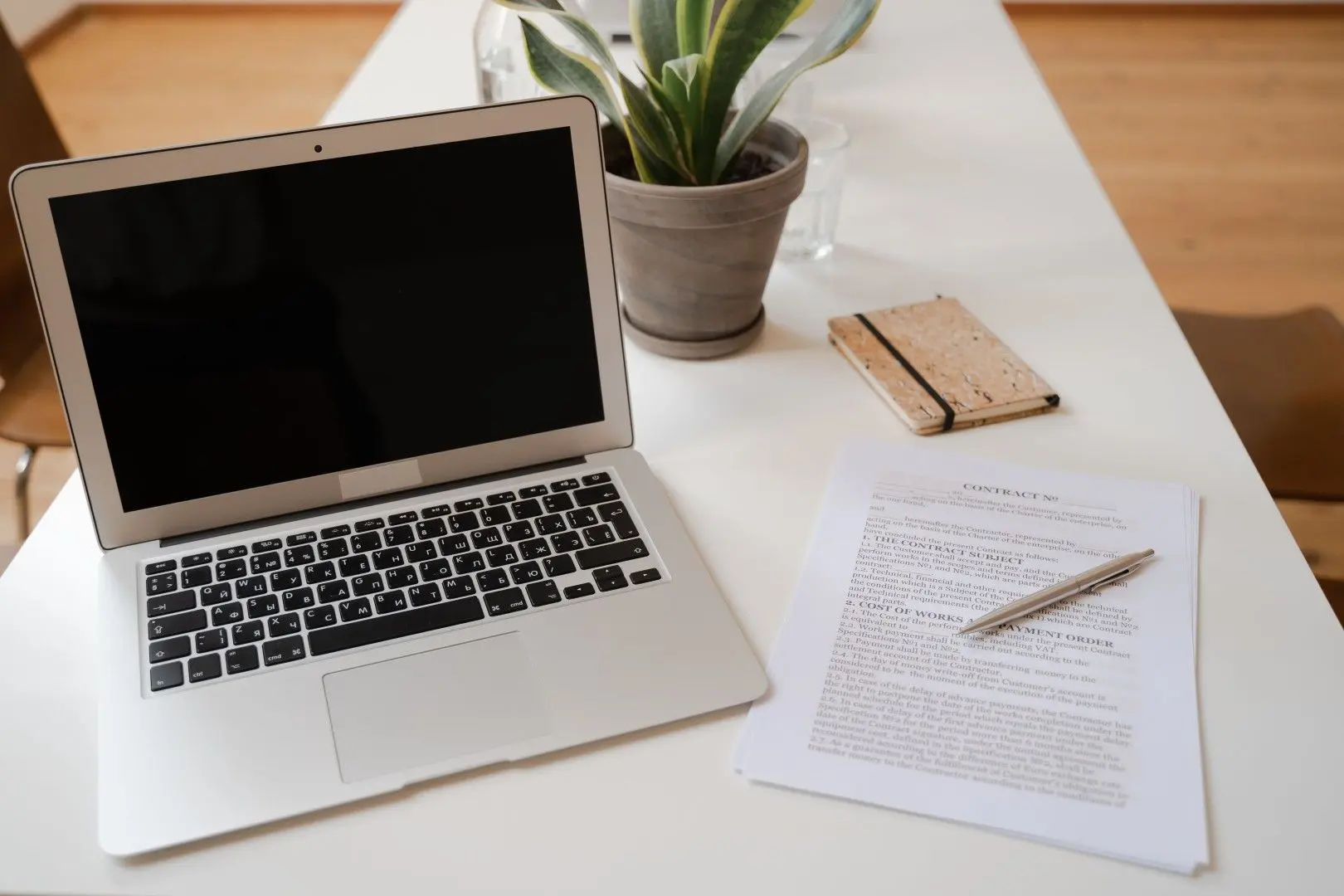 Un contrat de mission et un stylo posés sur un bureau blanc à côté d'un ordinateur portable.
