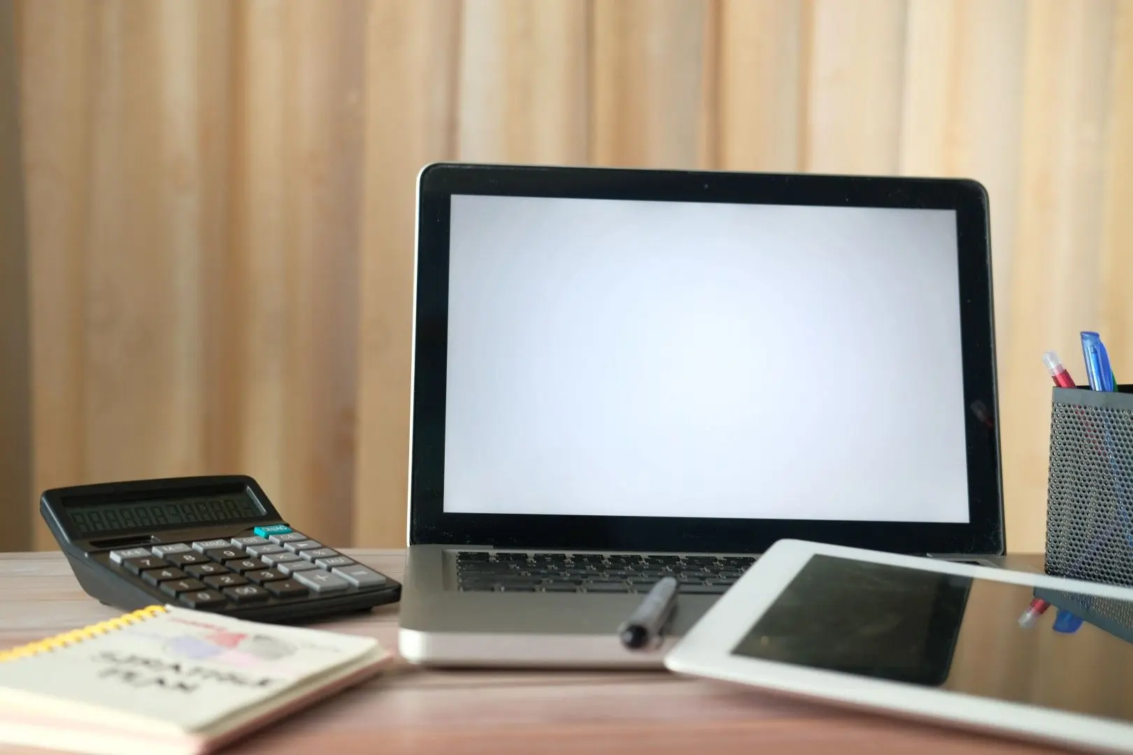 Ordinateur portable, calculatrice, tablette et carnet de notes posés sur un bureau.