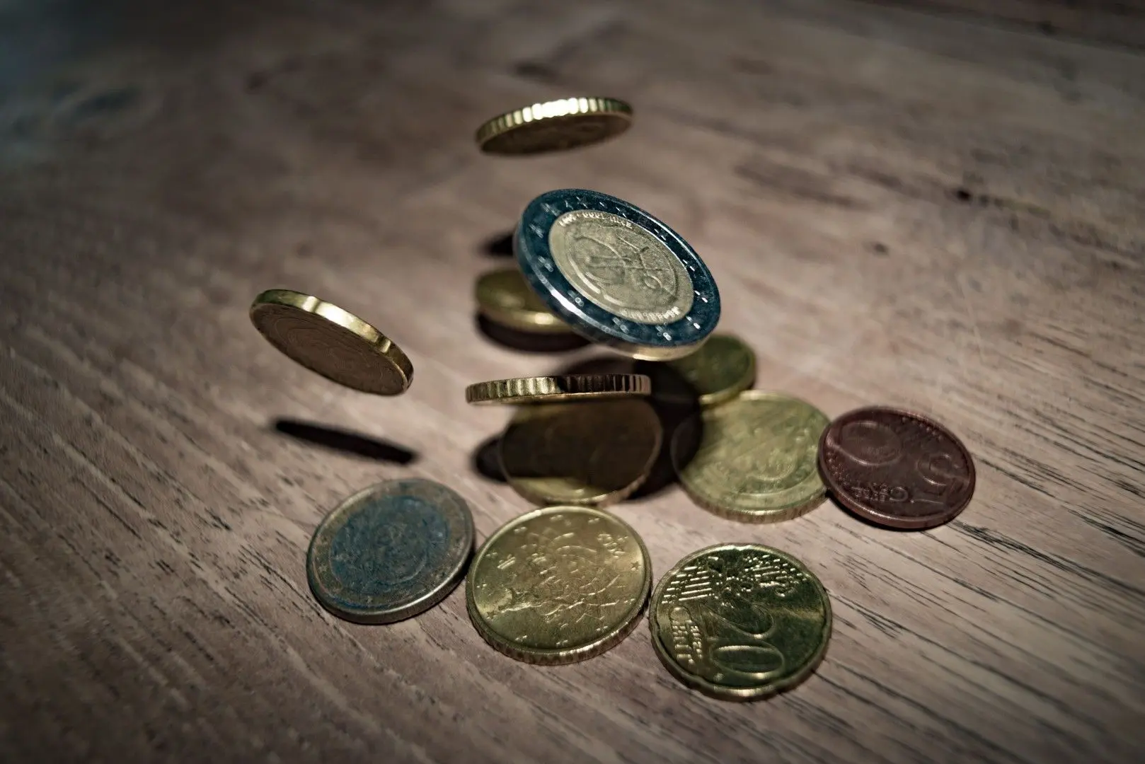 Pièces d'euros tombant sur une table en bois, symbolisant le versement d'un acompte sur salaire en intérim.