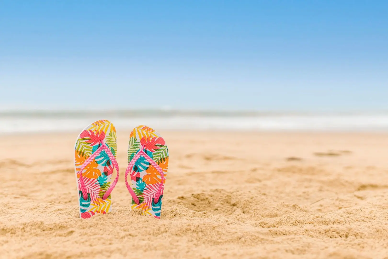 Paire de tongs colorées plantées dans le sable d’une plage face à la mer.