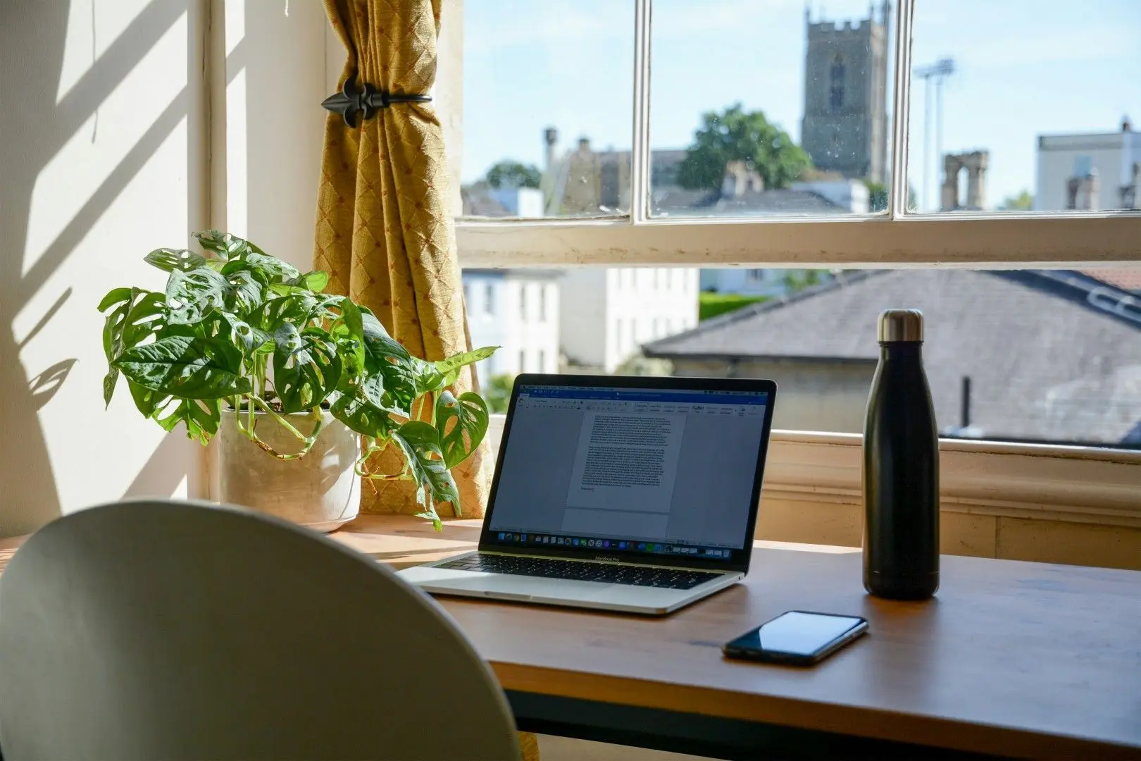 Espace de télétravail lumineux avec un ordinateur portable, un smartphone et une plante verte devant une fenêtre.