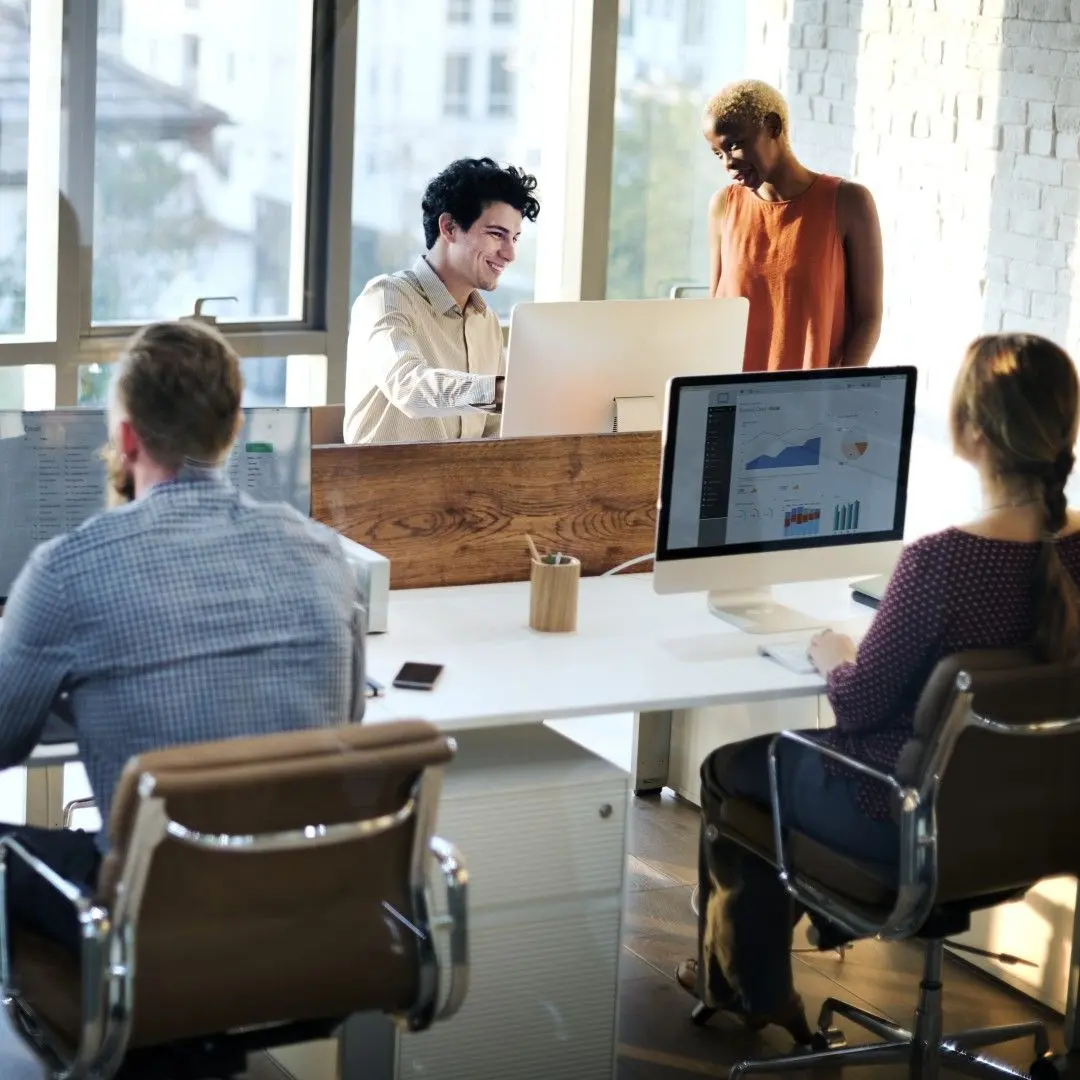 Des collaborateurs échangent et travaillent sur ordinateur dans un bureau moderne et lumineux.