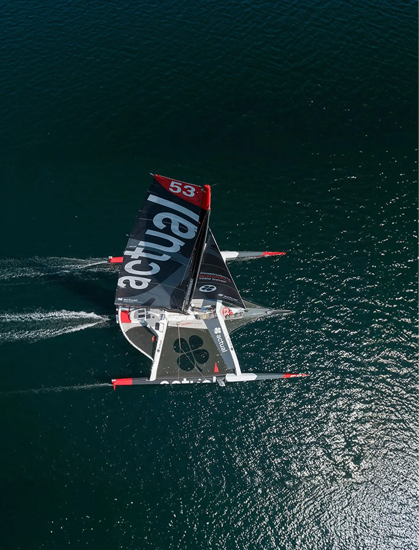 Vue aérienne du trimaran géant Ultim Actual naviguant en pleine mer.