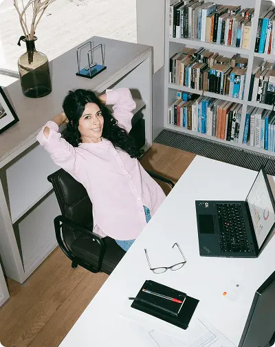 Une collaboratrice souriante, les mains derrière la tête, assise à son bureau devant un ordinateur portable.