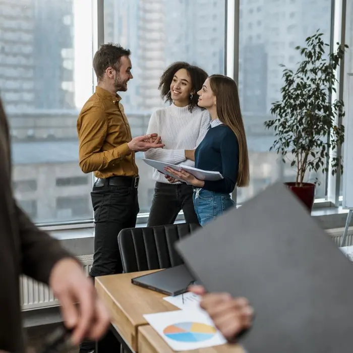 Trois collaborateurs échangent avec le sourire dans un bureau lumineux donnant sur la ville.