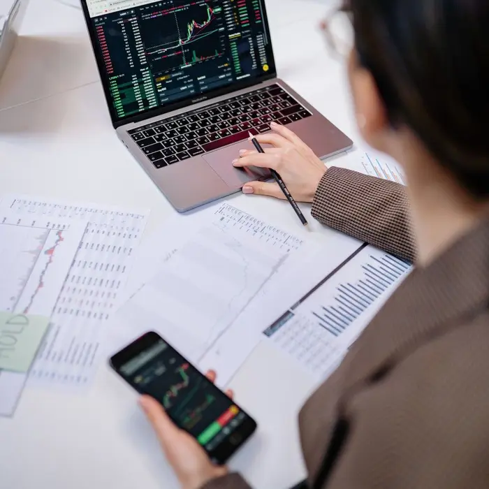 Une femme analyse des graphiques professionnels sur son ordinateur portable, son smartphone et des documents.