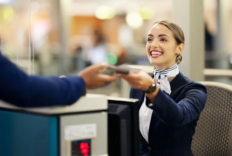 Une agente d'escale souriante remet un passeport à un voyageur au comptoir d'enregistrement.